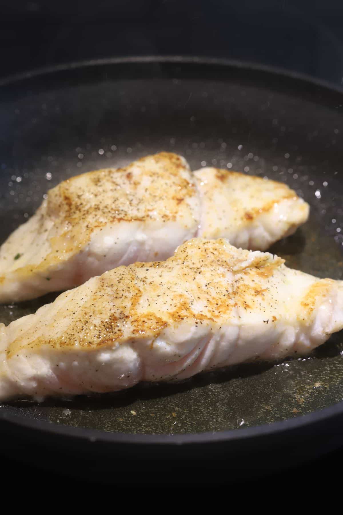 Two grouper fillets cooking in a skillet.