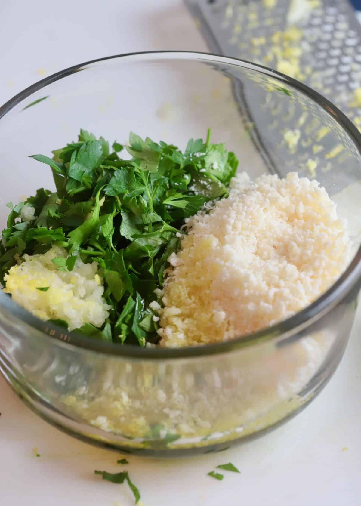 Gremolata ingredients in a bowl including lemon zest and parsley.