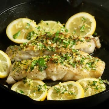 Cooked fish fillets topped with gremolata and garnished with lemon slices.