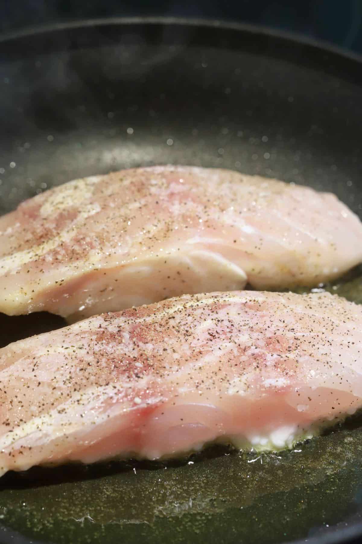 Pan-searing two grouper fillets in a skillet.