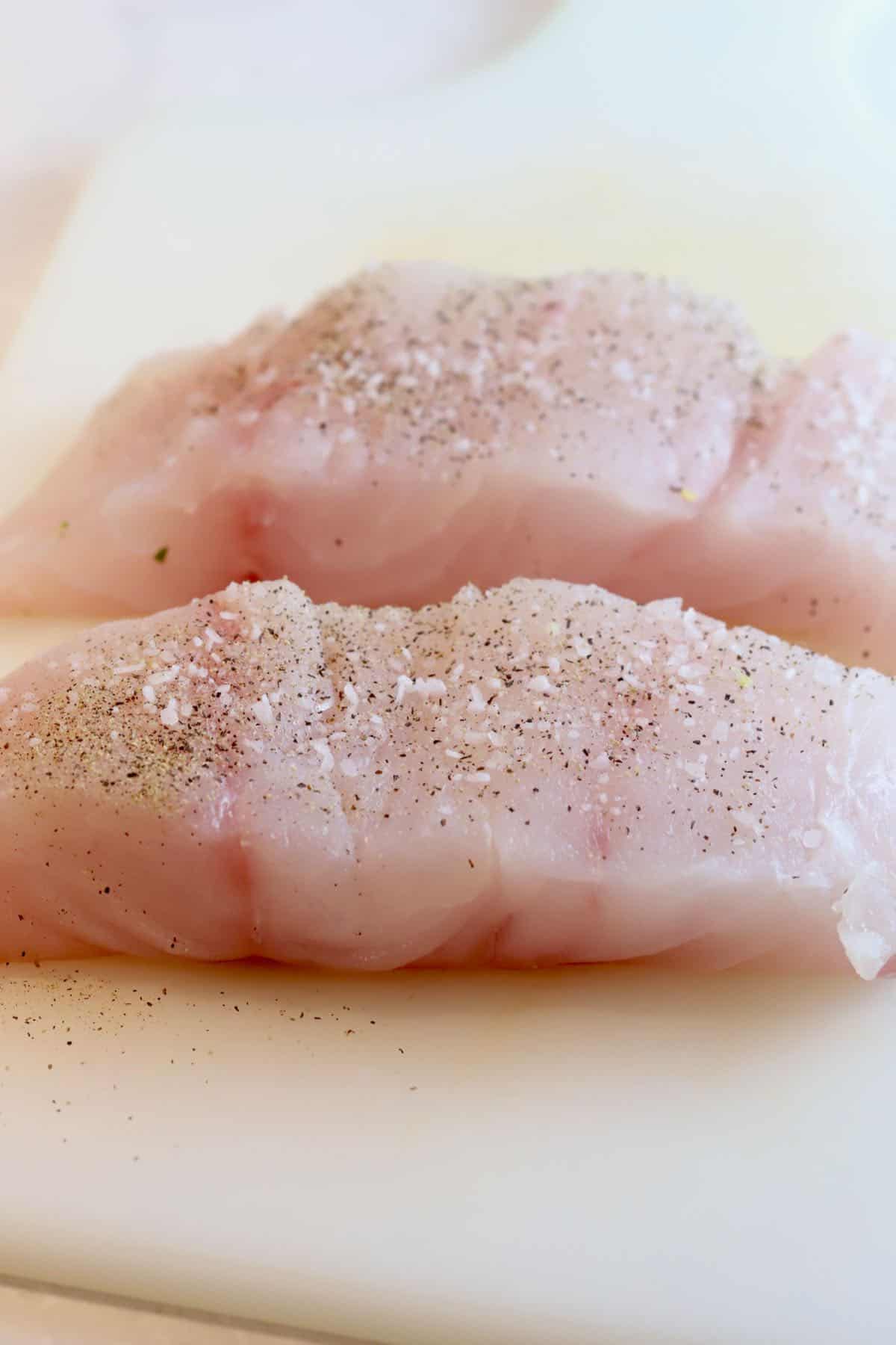 Two raw fish fillets seasoned with salt and pepper. 