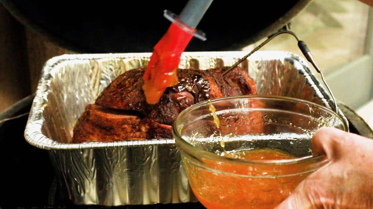 Using a pastry brush to top a ham with peach glaze.