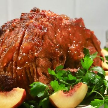 Smoked ham on a platter garnished with peach slices and parsley.