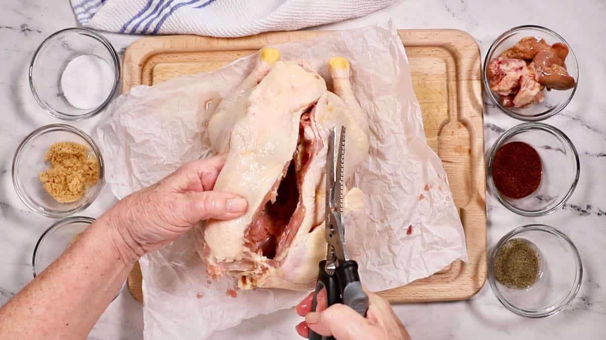 Using poultry shears to cut the backbone out of a chicken.