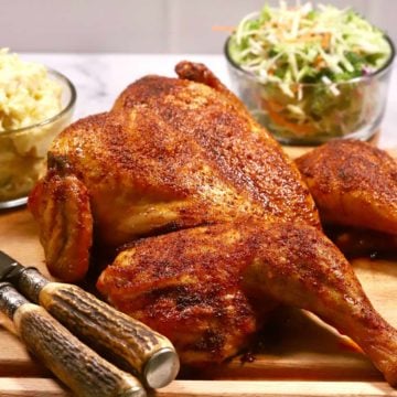 Smoked spatchcock chicken on a cutting board with carving utensils.