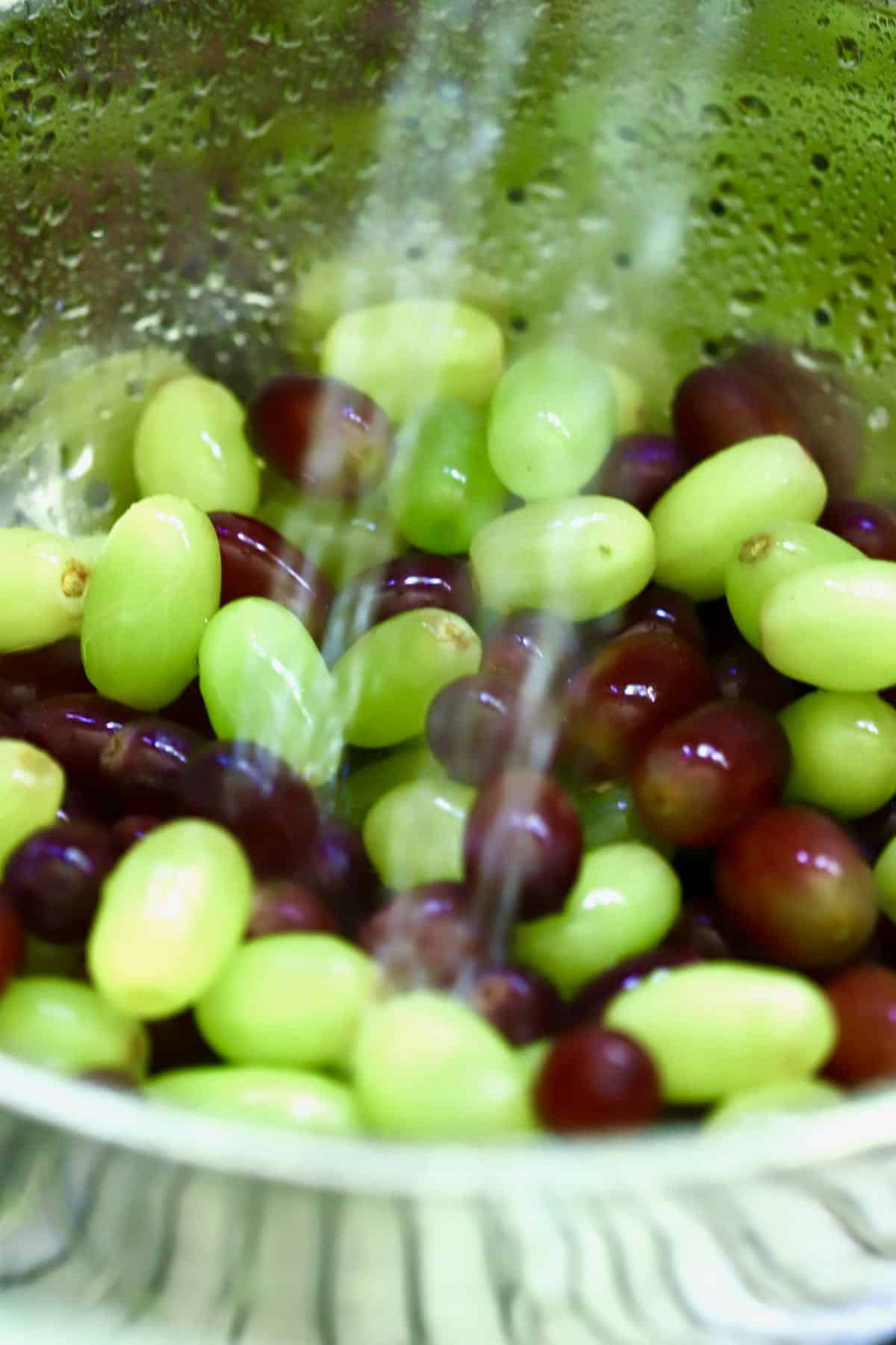 Grapes in a colander under running water in a sink.