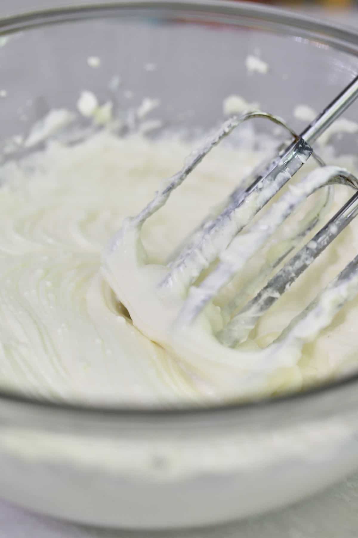 A glass mixing bowl with cream cheese being mixed up.