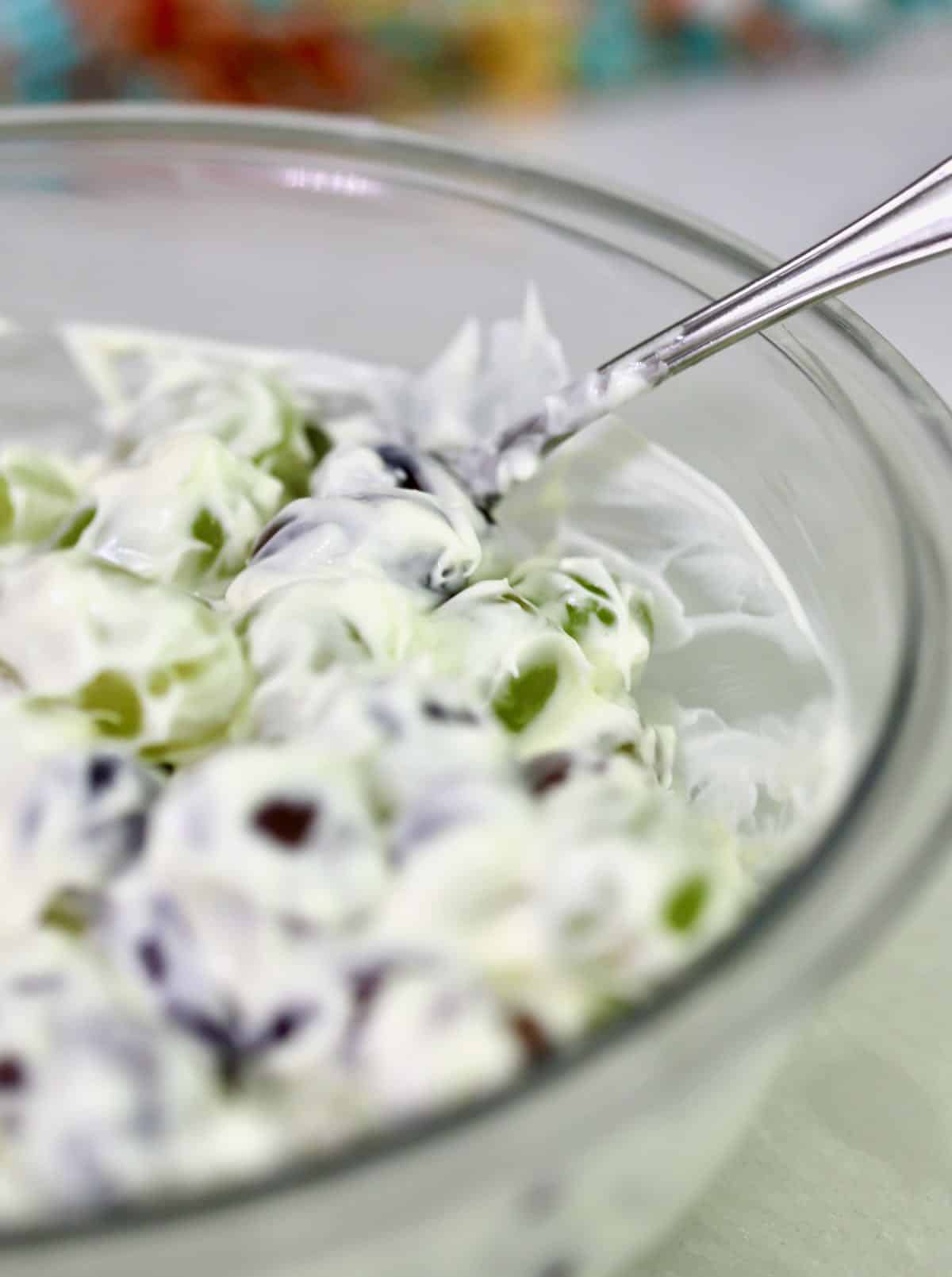 Mixing cream cheese and sour cream with grapes in a bowl.