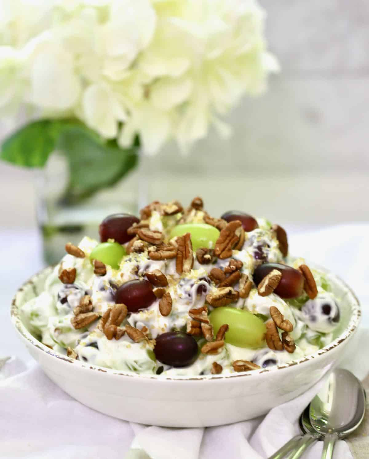 Grape salad topped with pecans and brown sugar in a white bowl. 