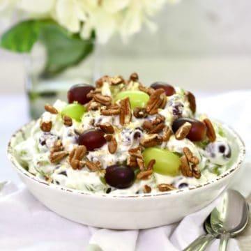Grape salad topped with pecans and brown sugar in a white bowl.