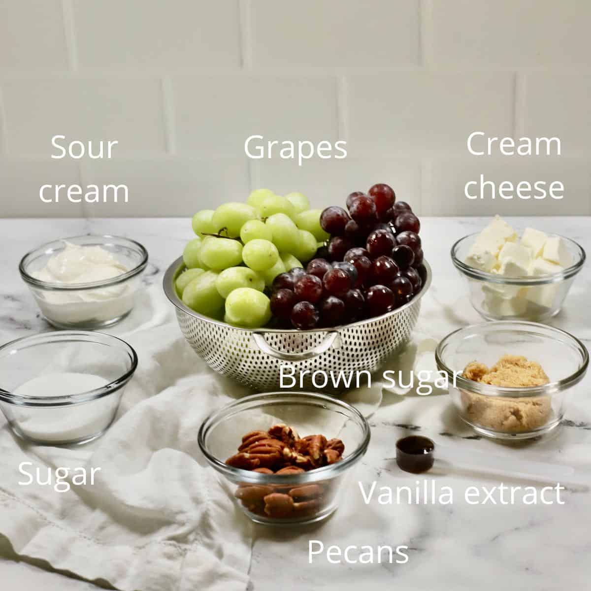 Grapes in a colander, and bowls of sugar, sour cream, and cream cheese. 