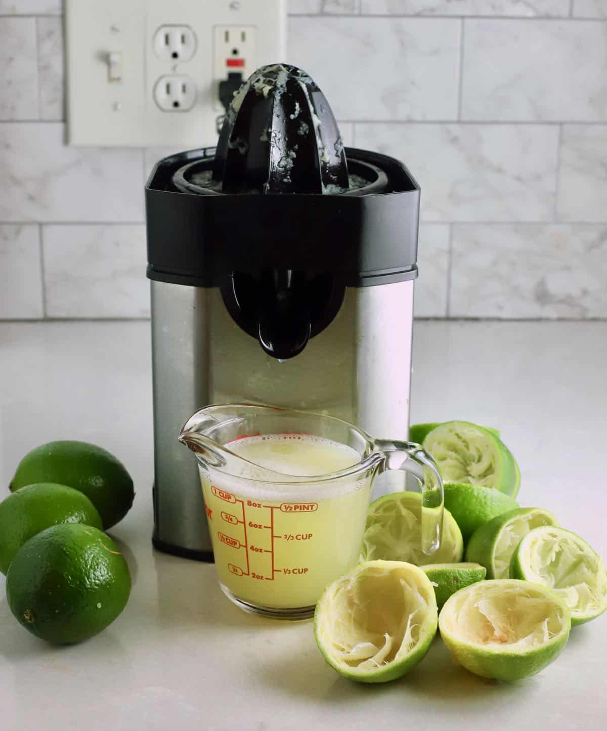 An electric juicer next to a measuring cup full of lime juice. 