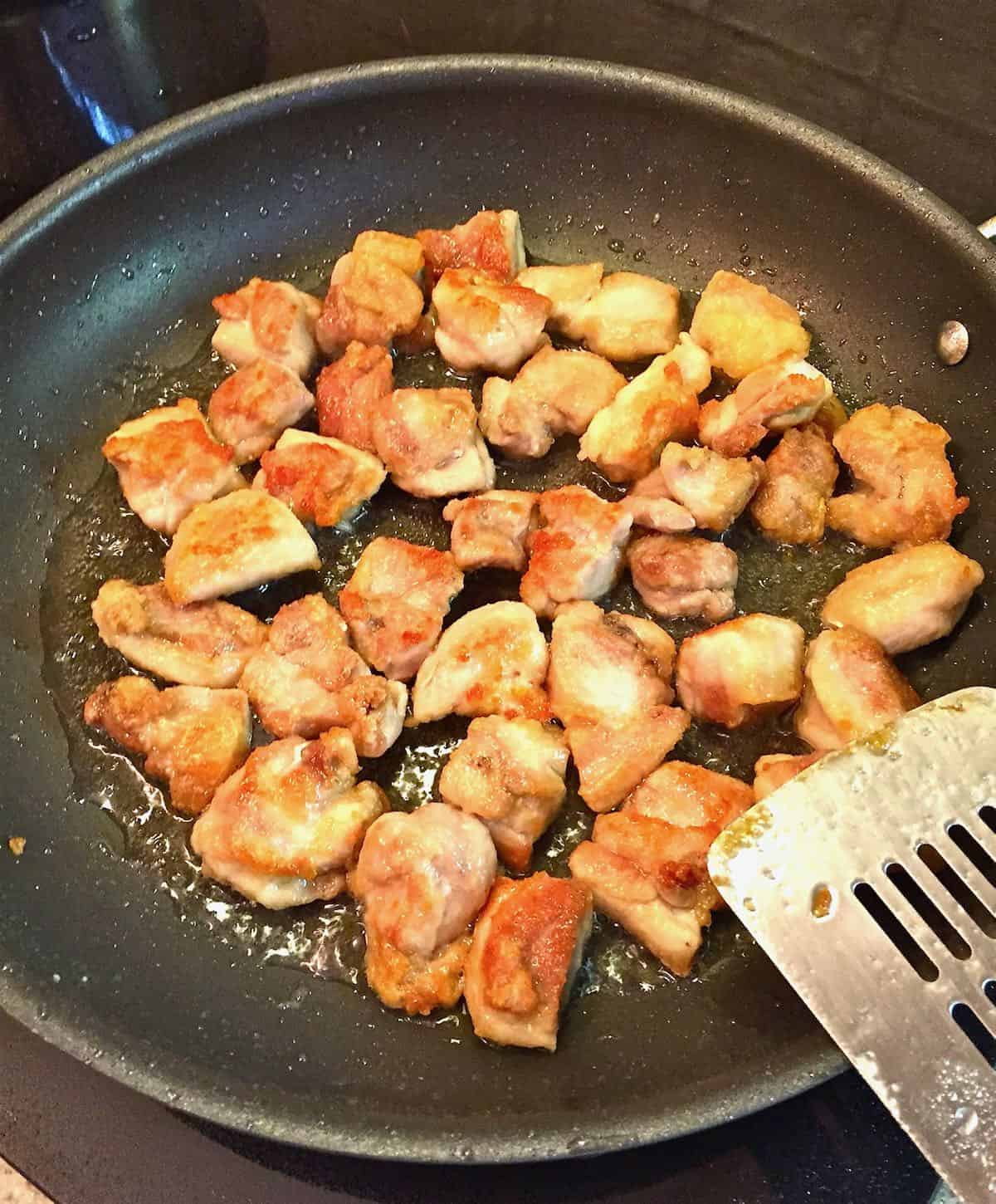 Pieces of chicken cooking in a skillet. 