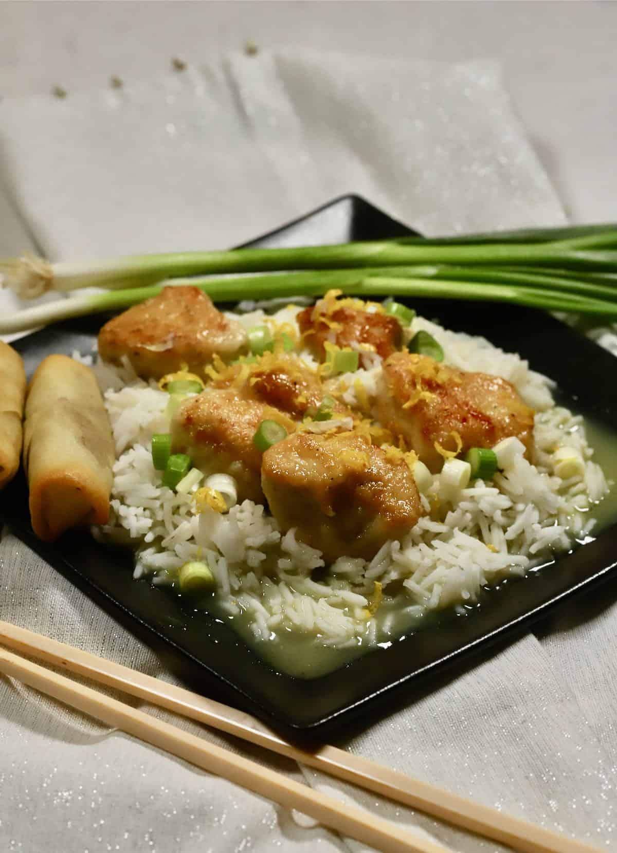 A black plate with rice topped with cooked pieces of chicken.