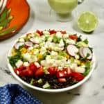 A large salad in a white bowl with a pitcher of dressing.
