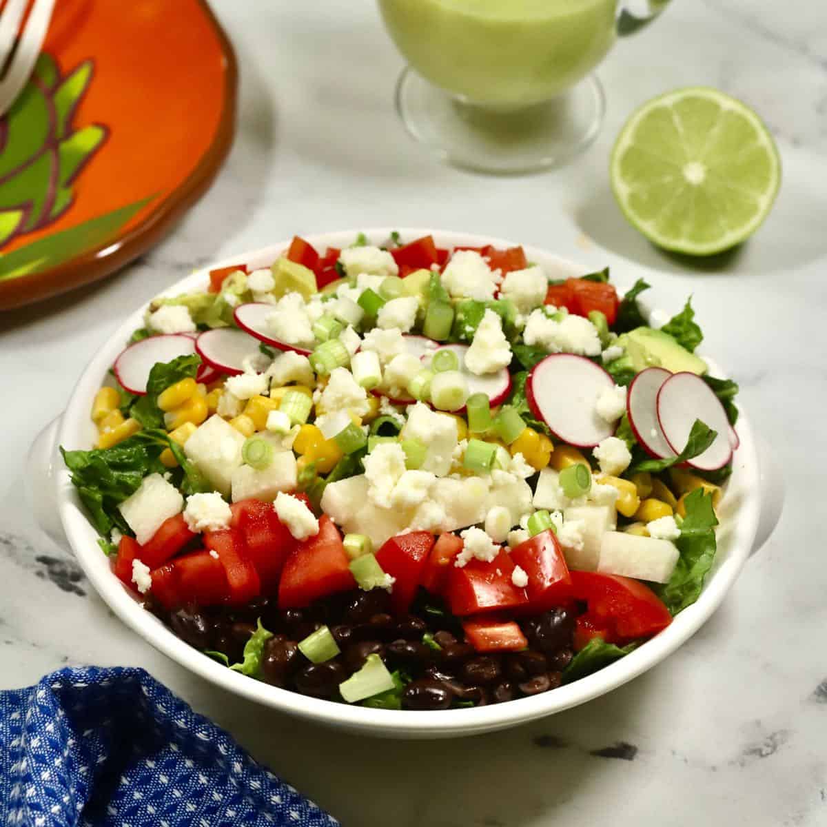 A large salad in a white bowl with a pitcher of dressing.