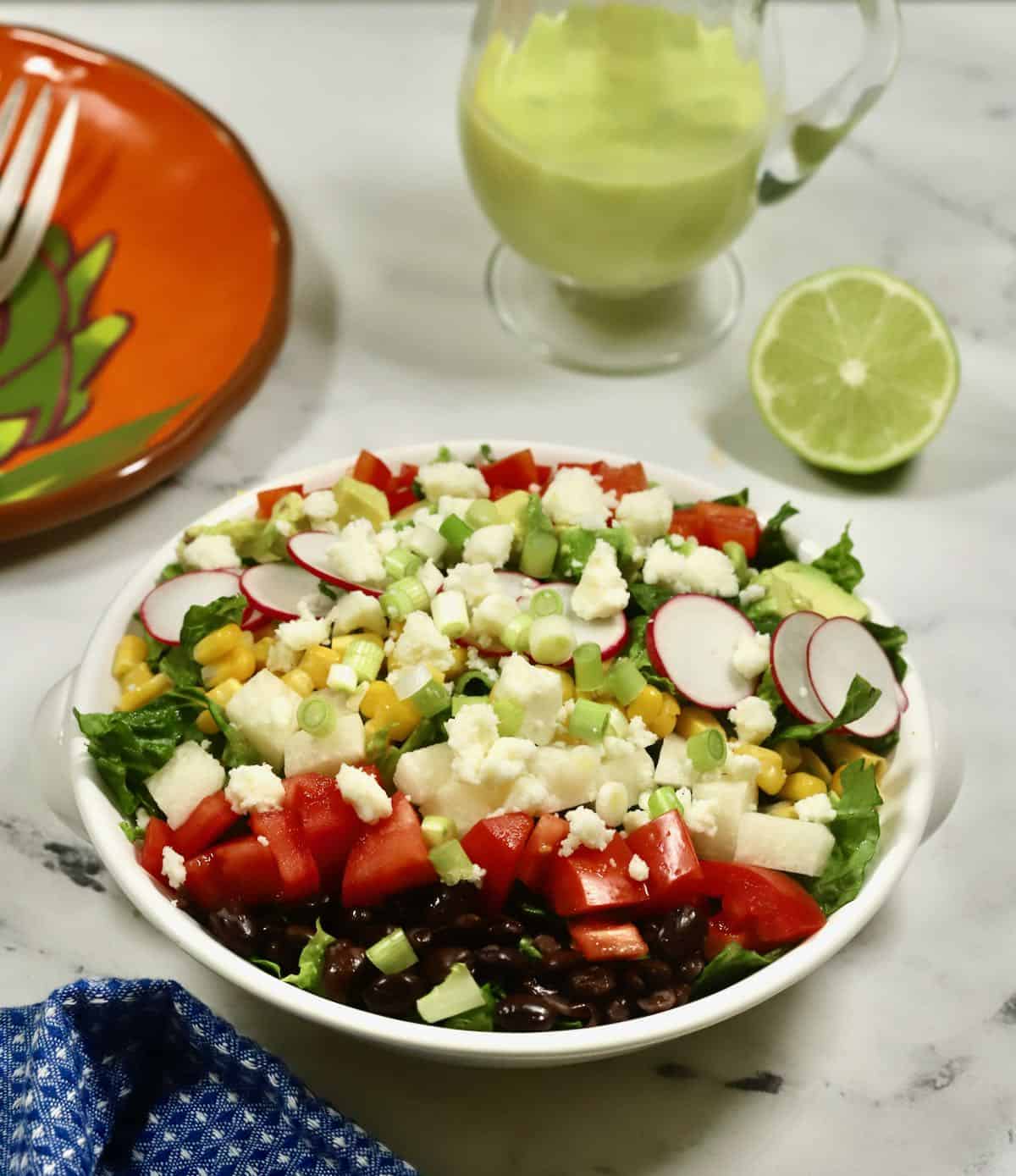 A large colorful salad with a small pitcher of dressing. 