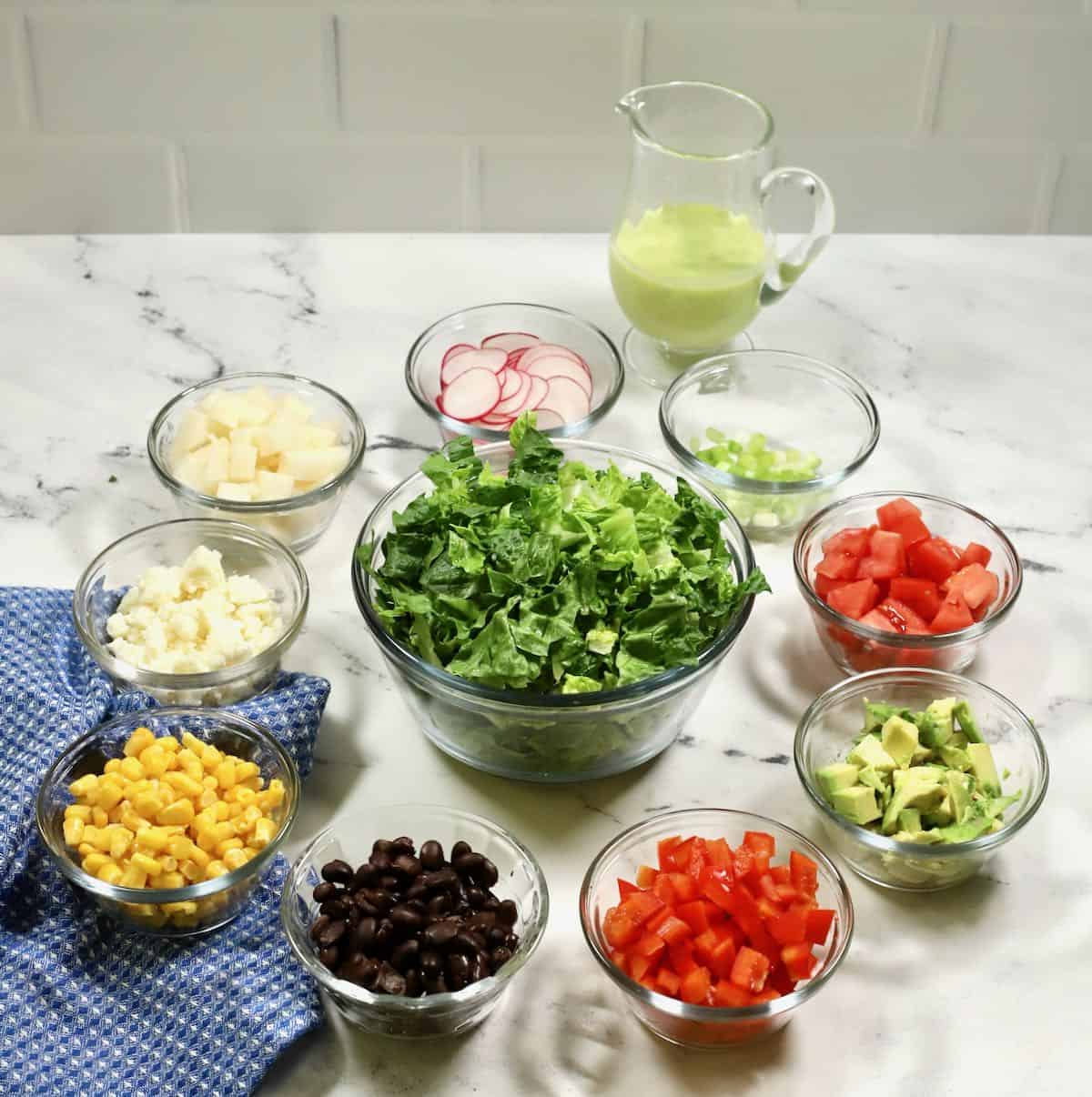 A large bowl of romaine lettuce plus other bowls of salad vegetables. 