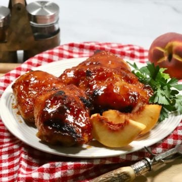 A white plate with smoked chicken thighs on top of a red and white kitchen towel.