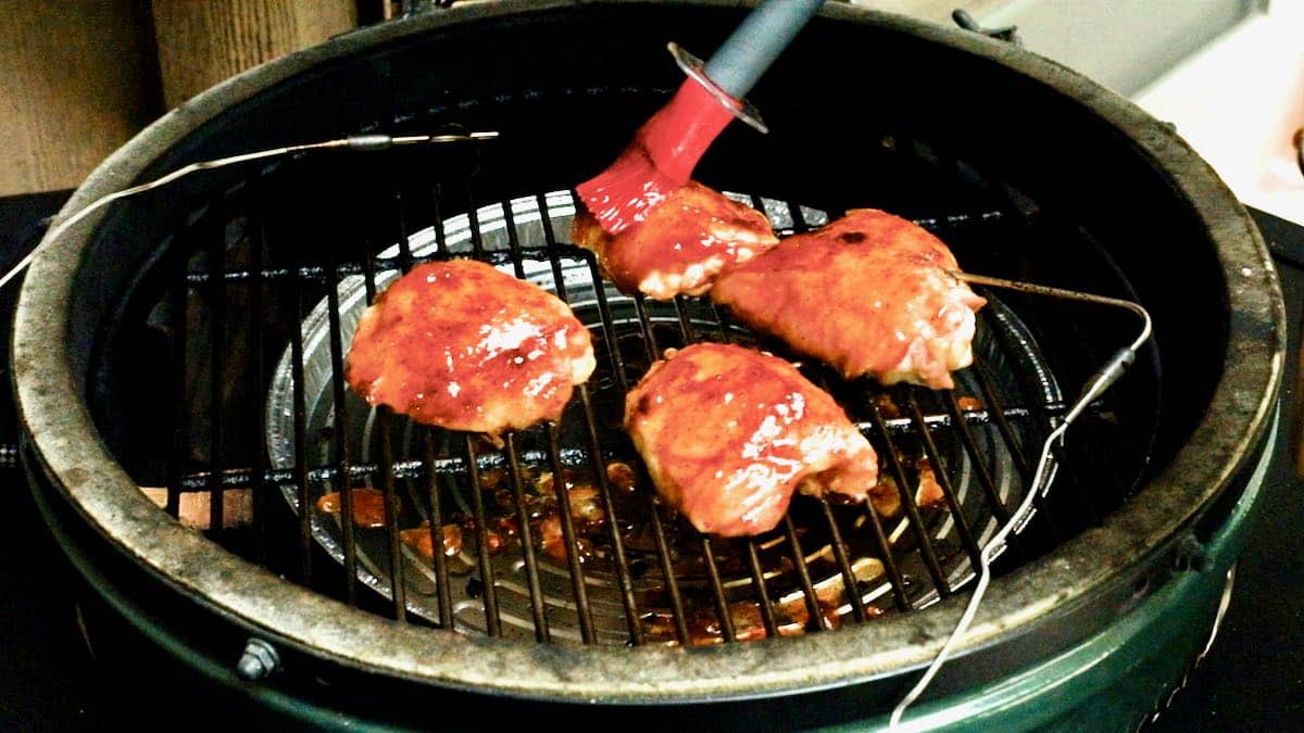 Brushing BBQ sauce on chicken cooking on a grill. 