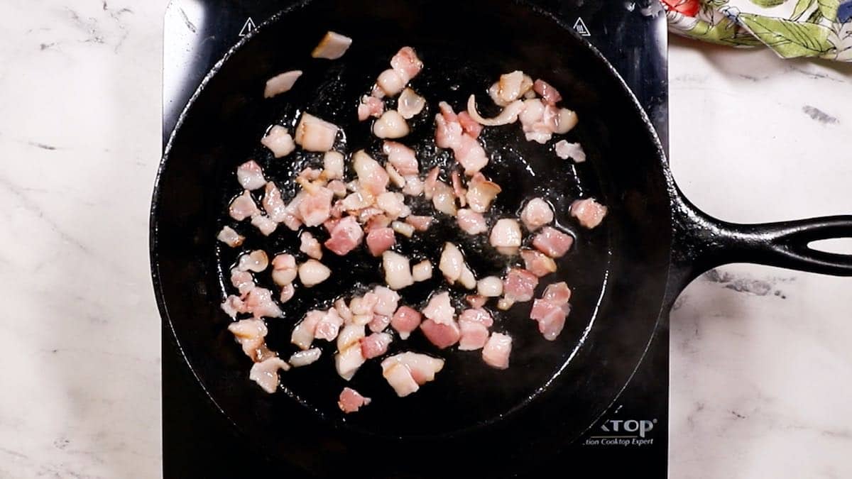 Chopped bacon frying in a cast-iron skillet.