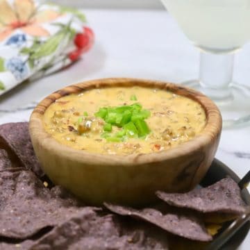 A wooden bowl with smoked queso dip and with chips.