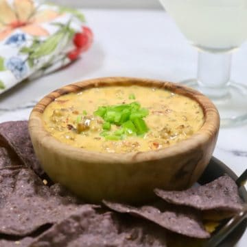 A wooden bowl with smoked queso dip and with chips.