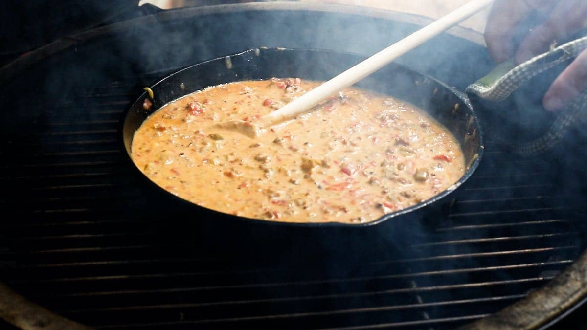 A cast-iron skillet containing queso in a Big Green Egg.