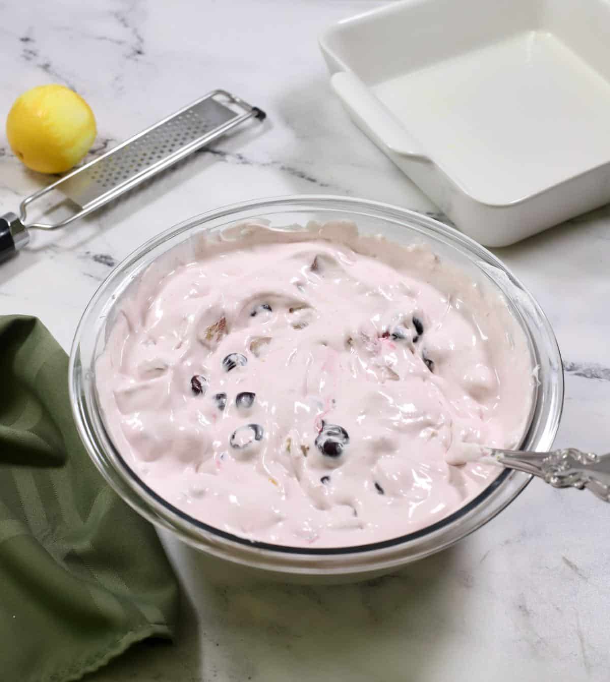 Cherries, pineapple and nuts mixed with frozen whipped topping in a bowl.