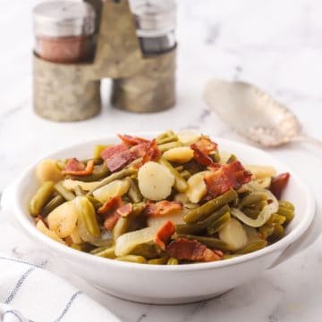 Sweet and sour green beans in a white bowl topped with bacon.