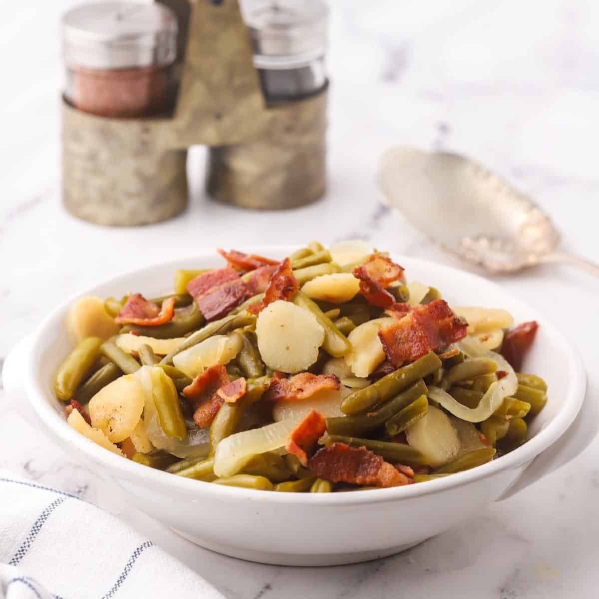 Sweet and sour green beans in a white bowl topped with bacon.