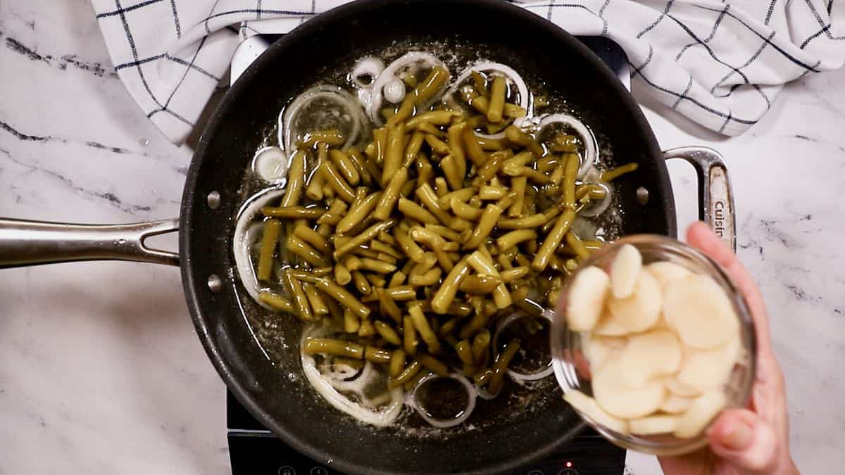 Adding sliced water chestnuts to green beans cooking in a skillet.