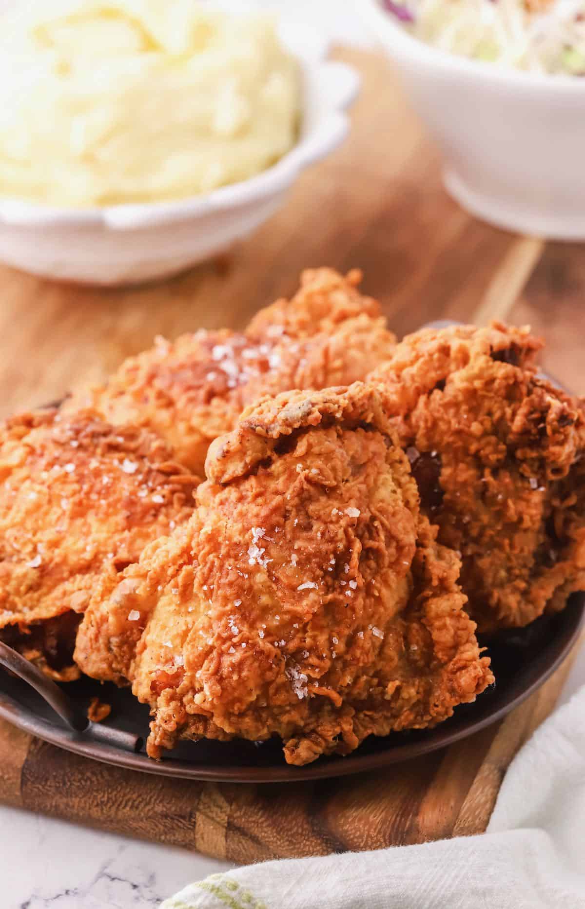Four pieces of fried chicken on a plate on a cutting board. 