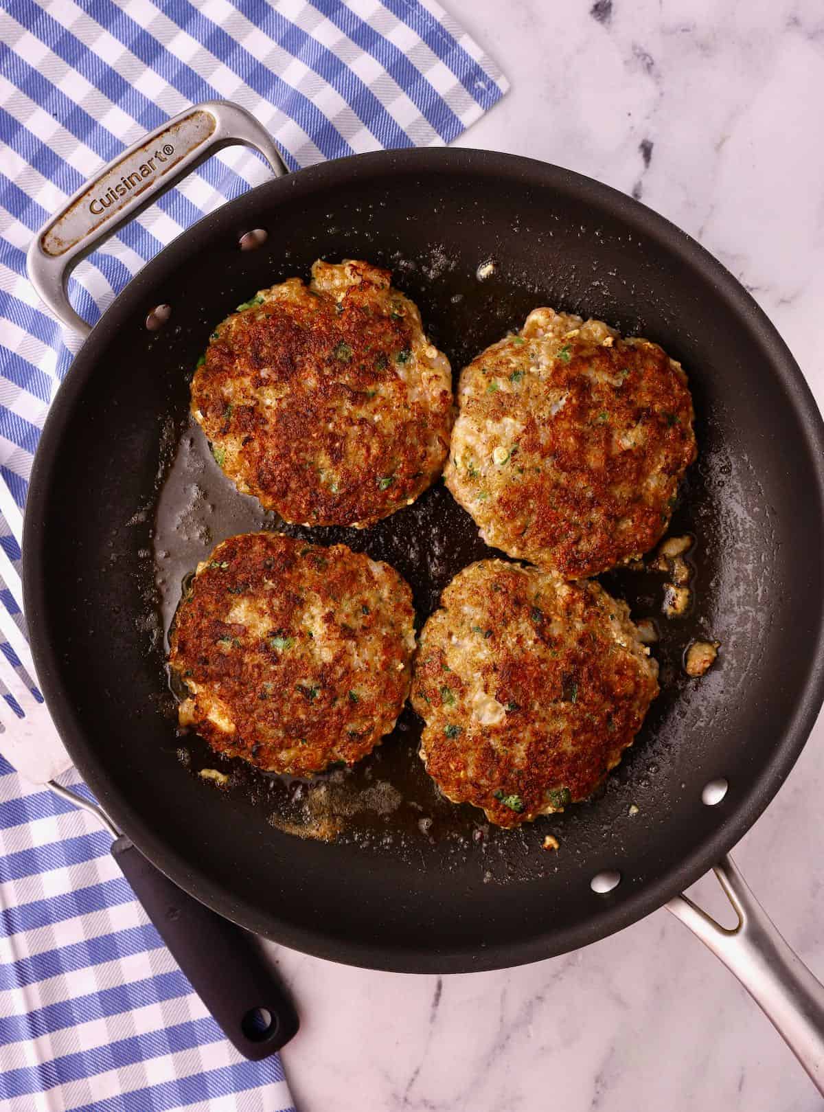 Four shrimp burgers cooking in a skillet. 