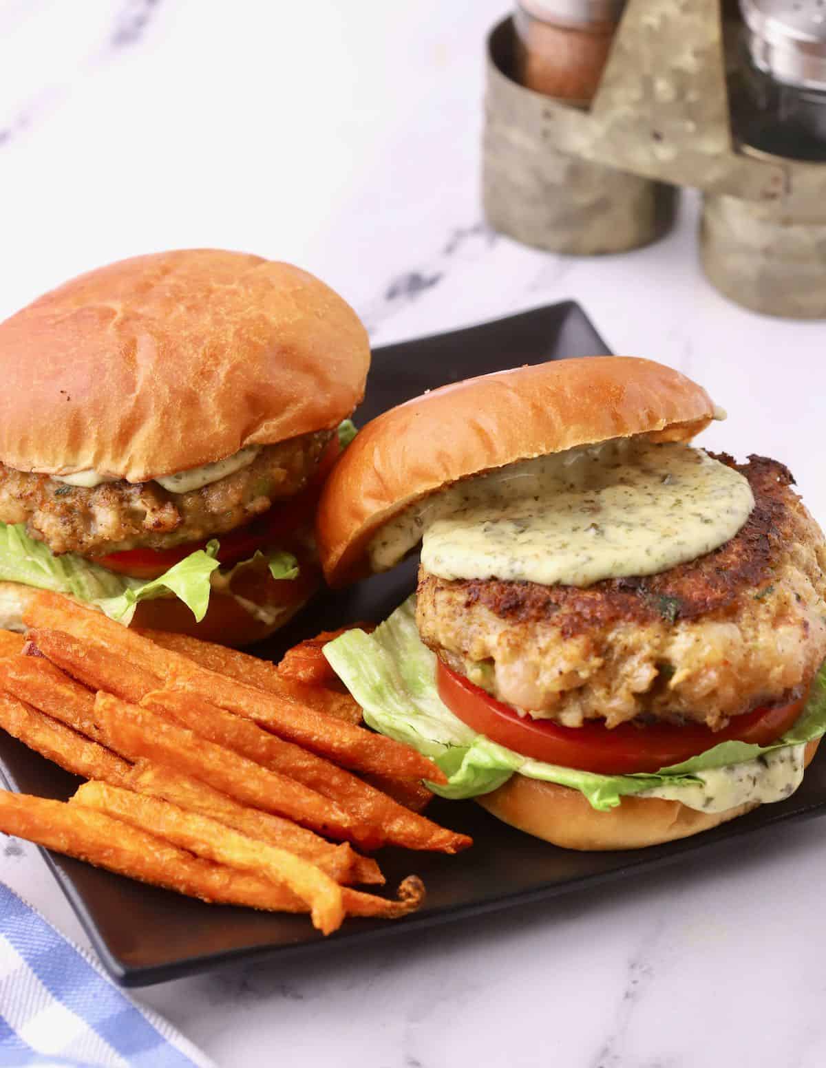 Two shrimp burgers on a black plate. 