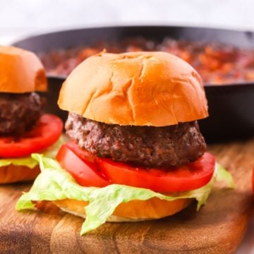 A burger with lettuce and tomato on a cutting board.