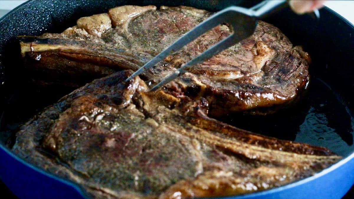 Two steaks being seared in a cast-iron skillet. 