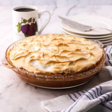 A whole banana pudding pie with plates and a cup of coffee.