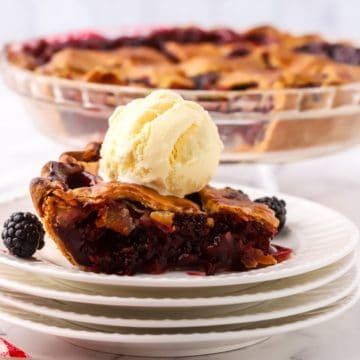 A slice of blackberry pie on a white plate topped with ice cream.