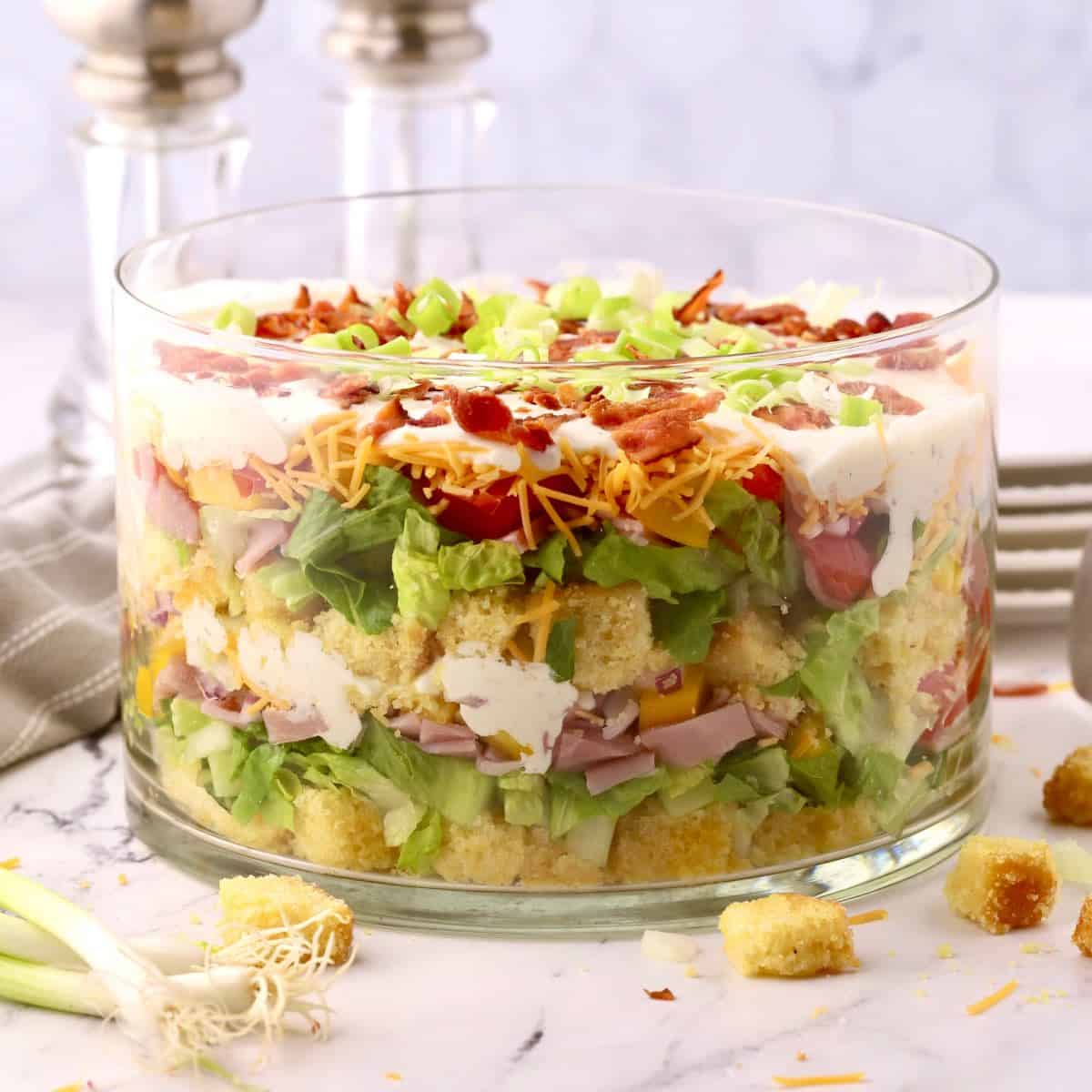 A glass trifle dish with a layered cornbread salad.