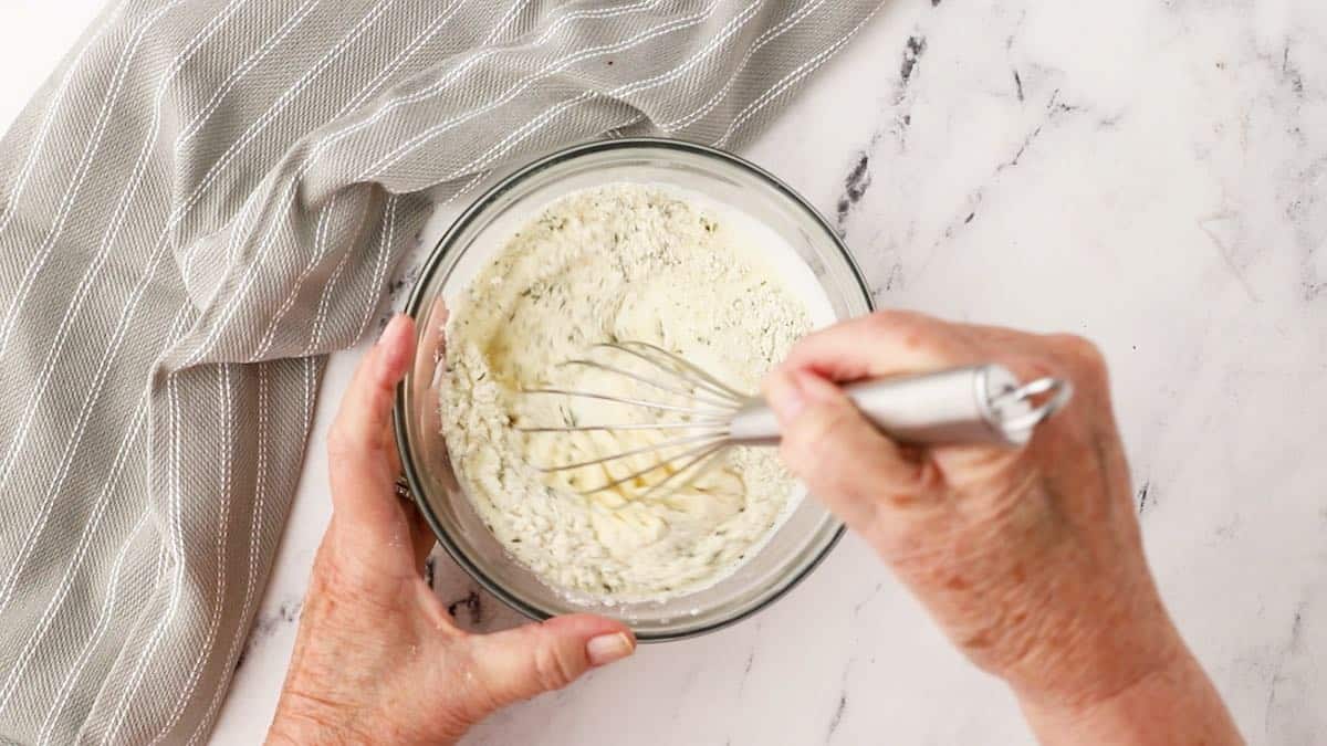 Mixing ranch dressing  with a whisk in a glass bowl. 