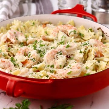 A red baking dish with shrimp pasta garnished with parsley.