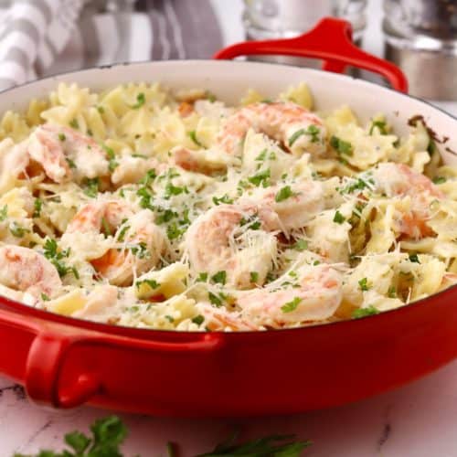 A red baking dish with shrimp pasta garnished with parsley.