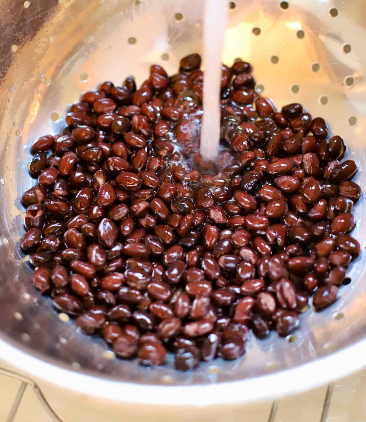 Black beans in a colander under running water.