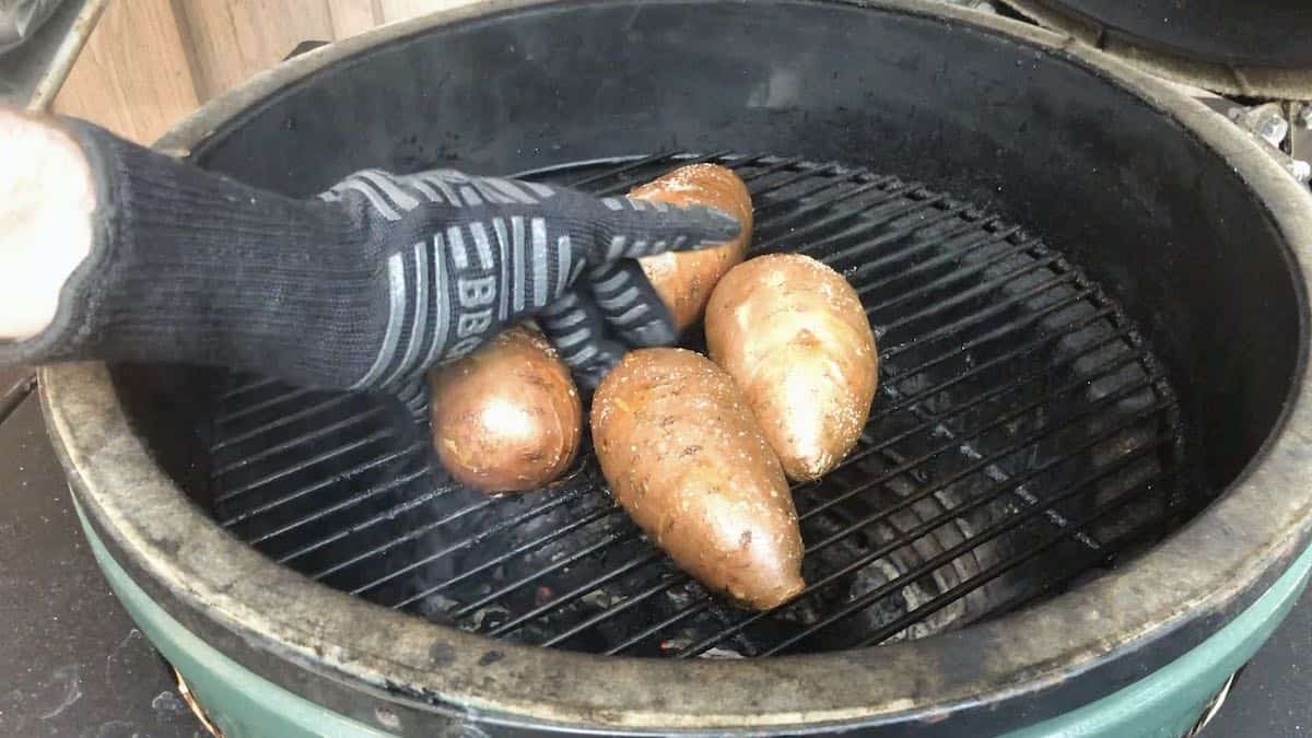 Squeezing sweet potatoes smoked on a grill to see if they are done. 