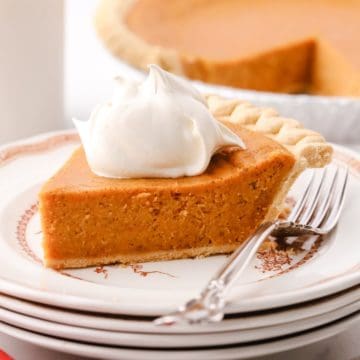A slice of sweet potato pie topped with whipped cream on a plate.
