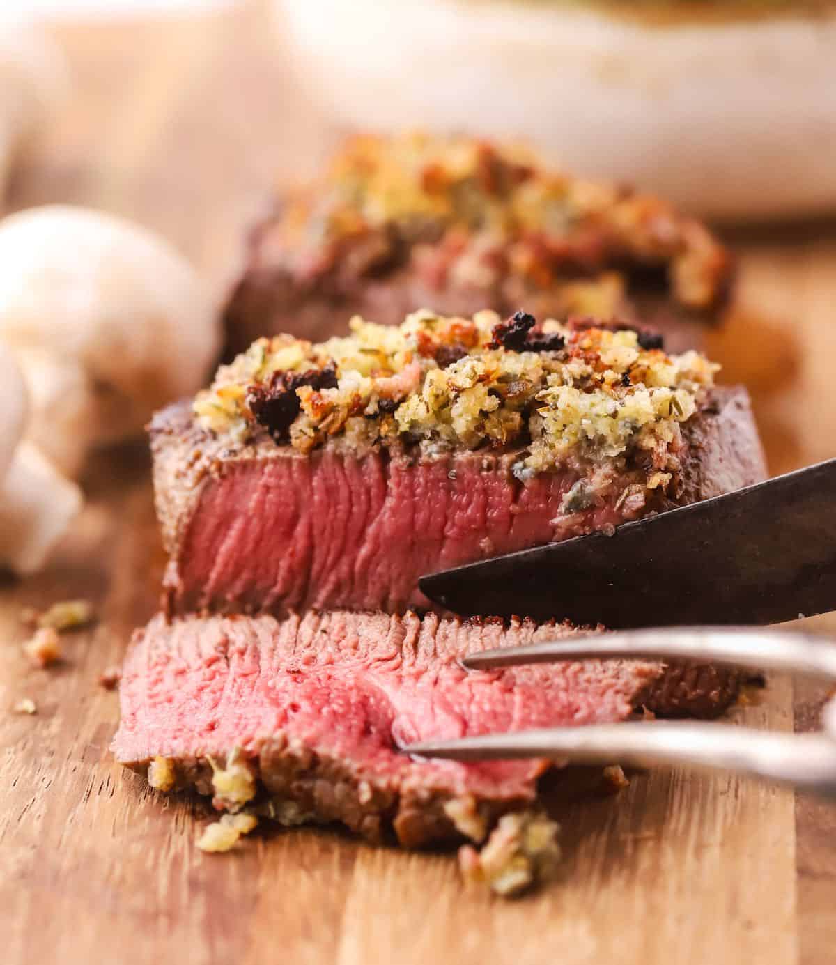 A filet mignon topped with blue cheese being sliced on a cutting board. 