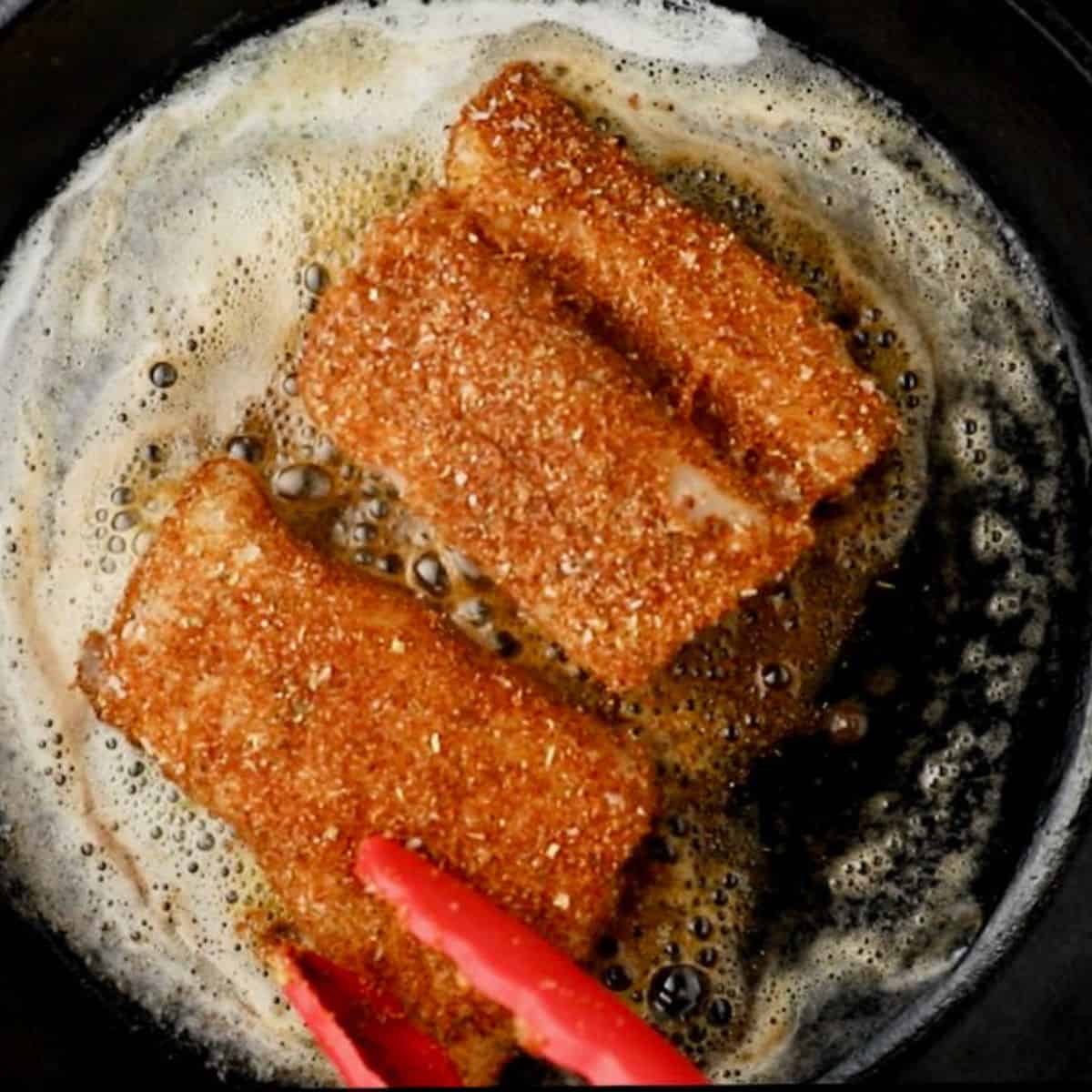 Two cod fillets are topped with blackening seasoning and cooked in a cast-iron skillet. 