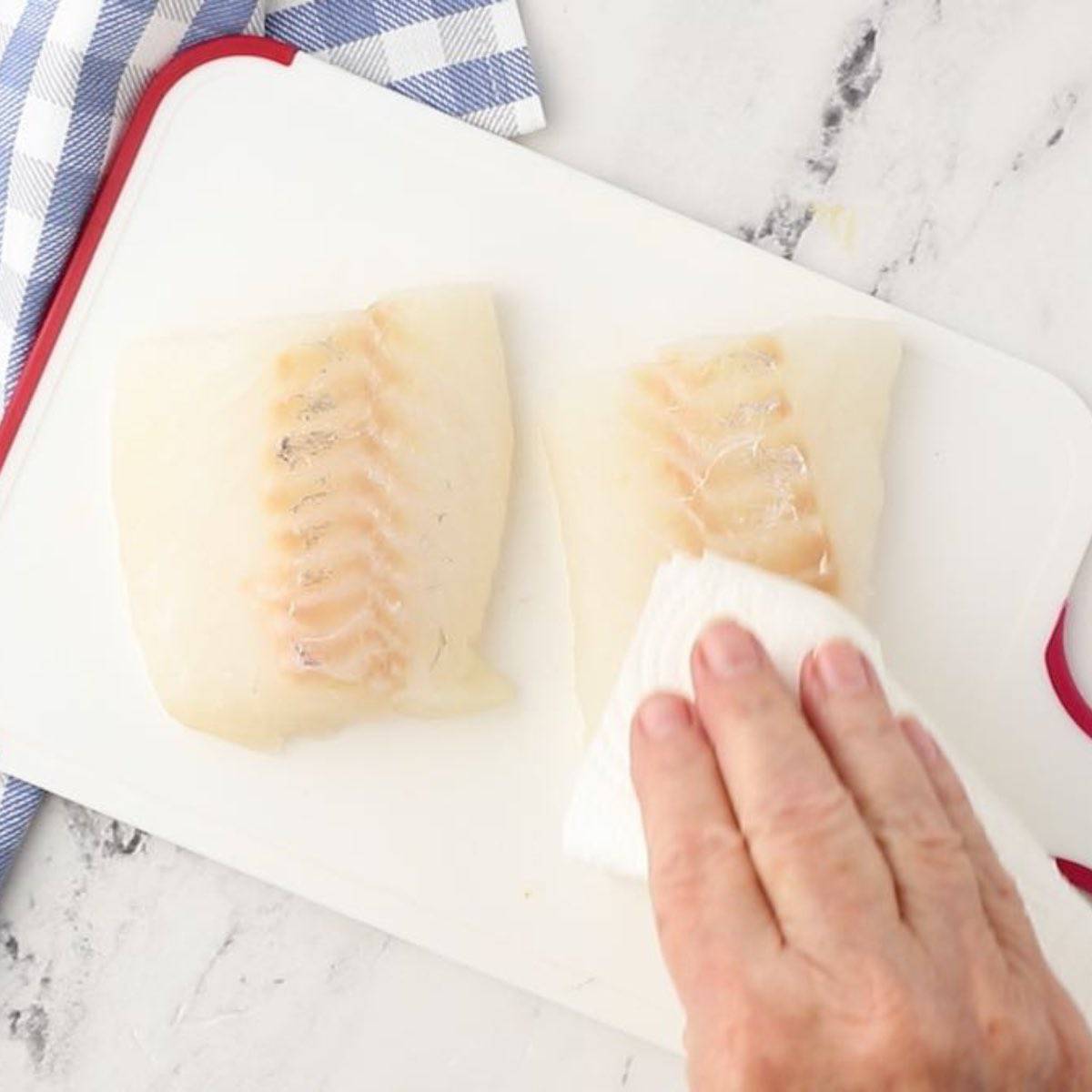 Using a folded-up paper towel to dry off cod fillets.