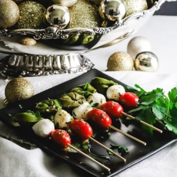 A black plate with five caprese skewers on it.